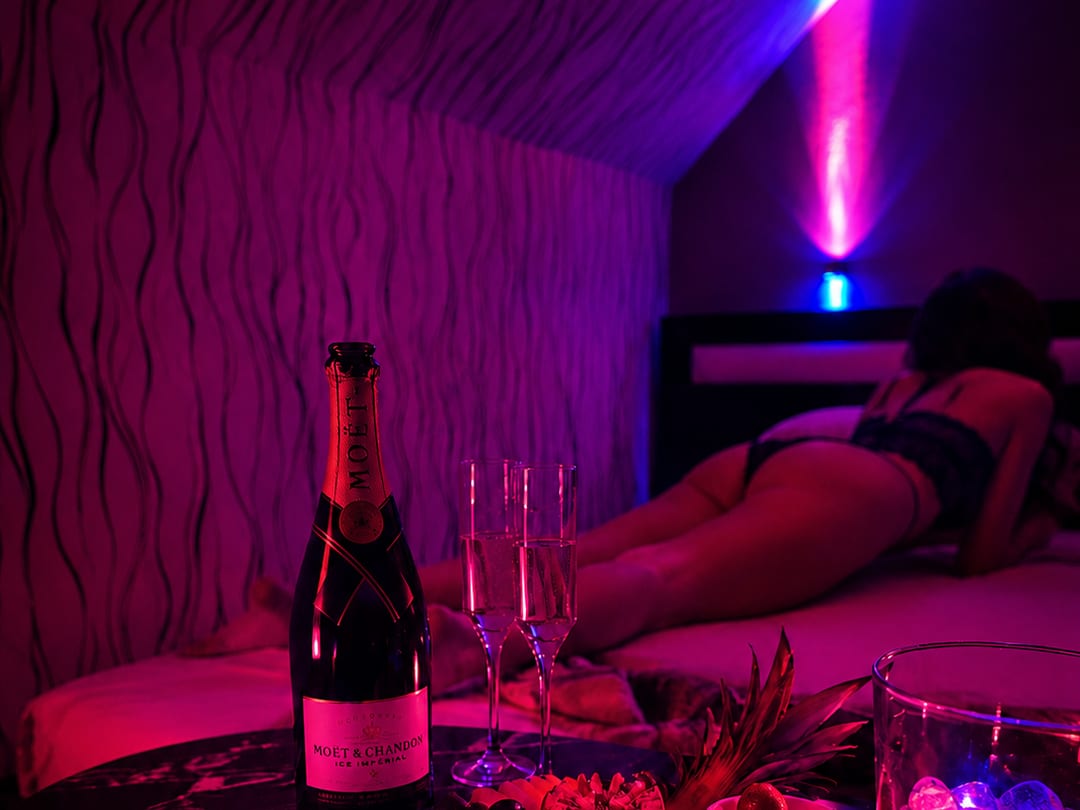 Privates Zimmer mit Bett, Sektflasche und magentafarbenem Licht